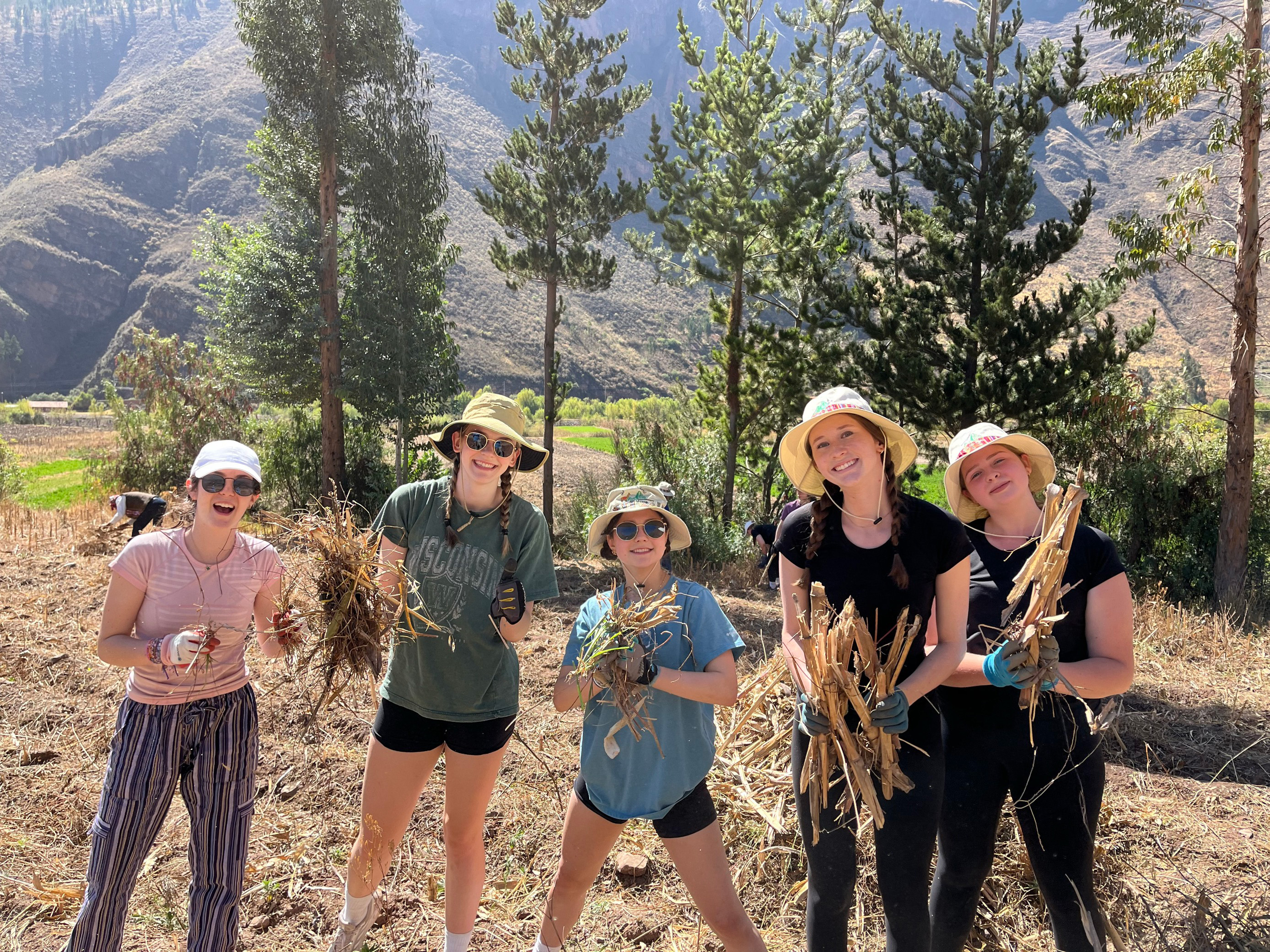 Five gloved students with hats hold plants in Peru.