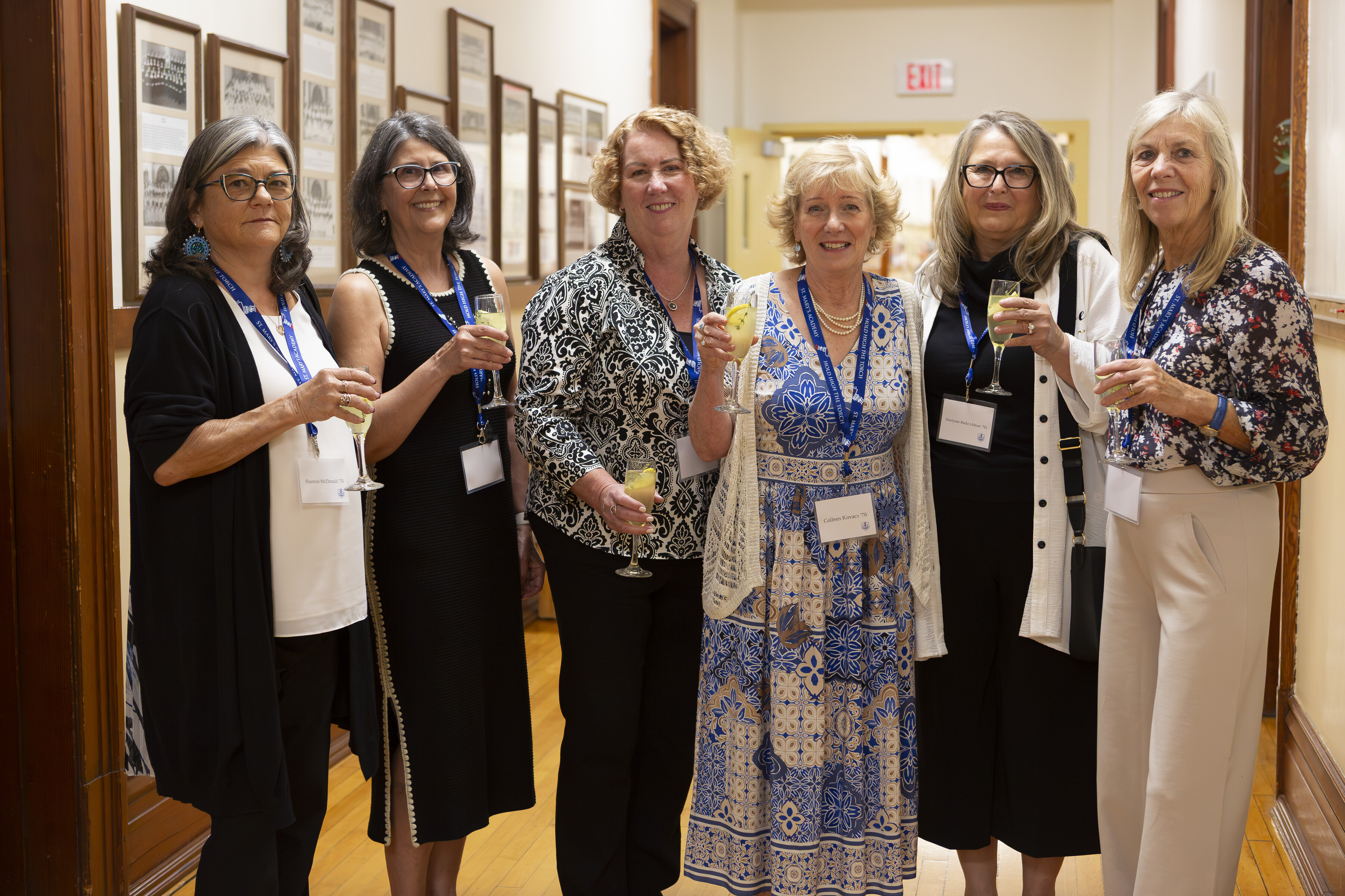Nine smiling former SMA faculty and staff stand in front of a St. Mary's Academy backdrop.