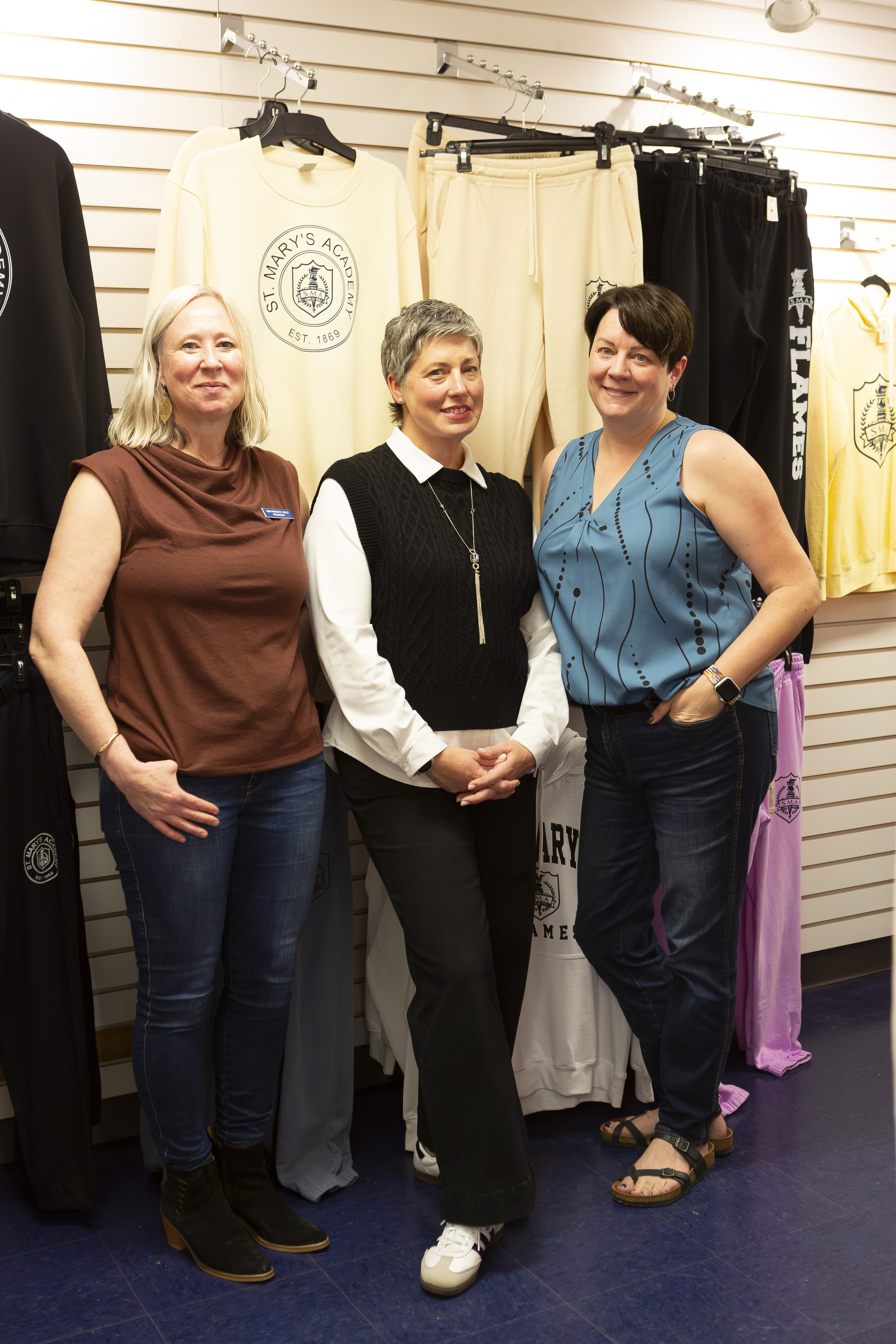 Three smiling adults stand amongst St. Mary's Academy merchandise