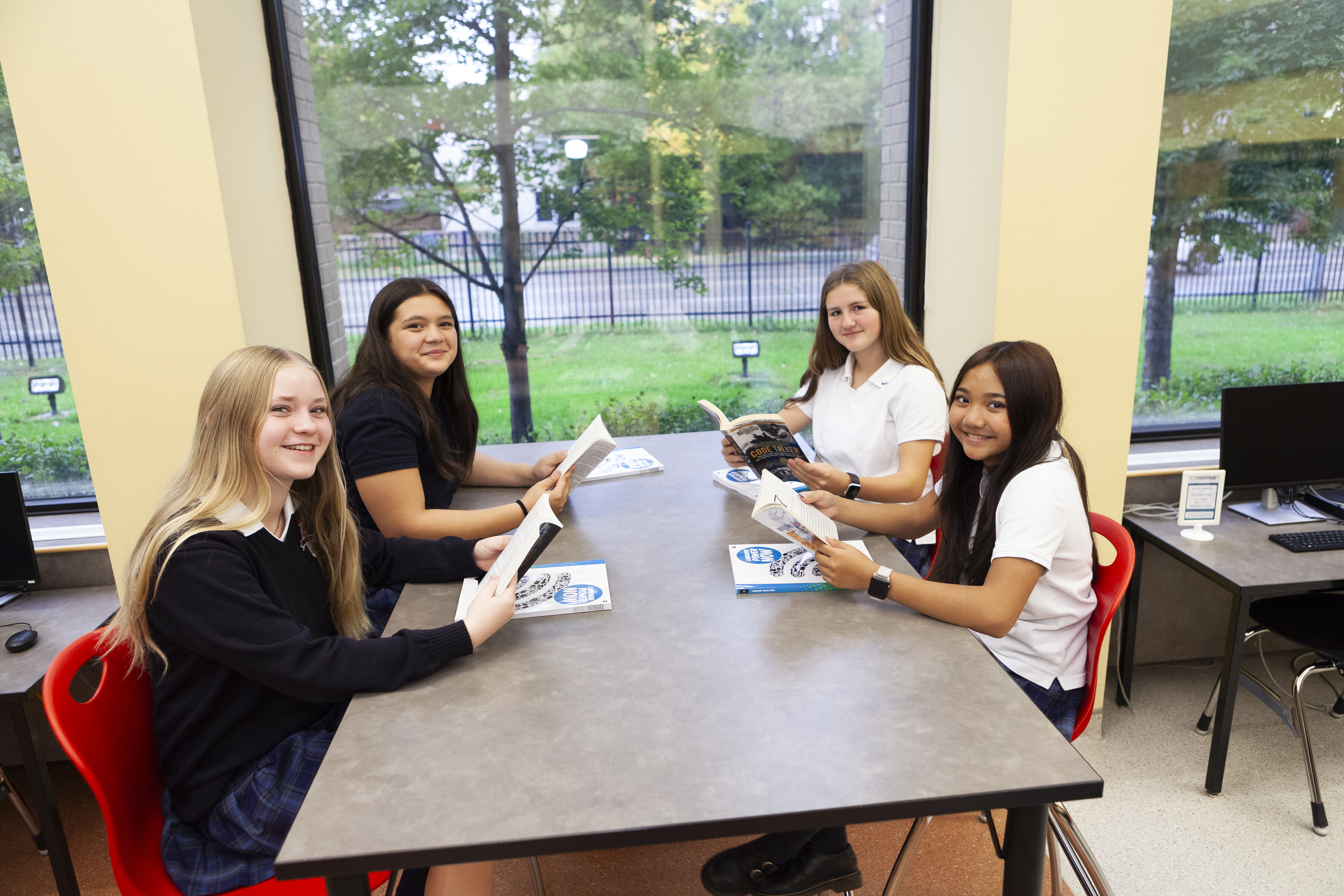 Four smiling students sitting around a table and holding books