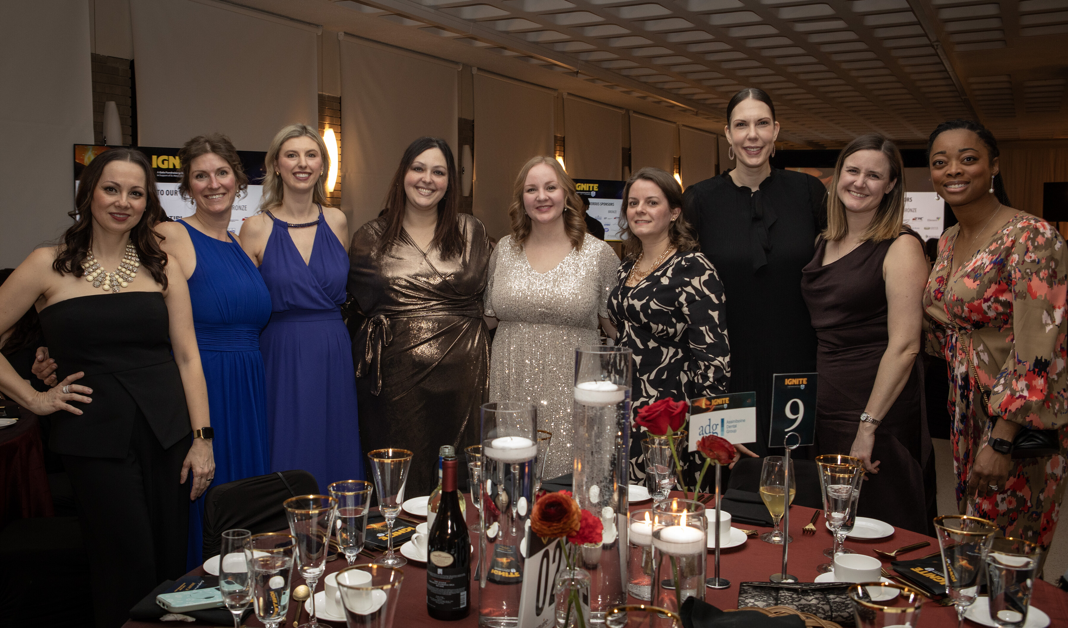 a group of women dressed in formal attire with a fancy table setting in the foreground
