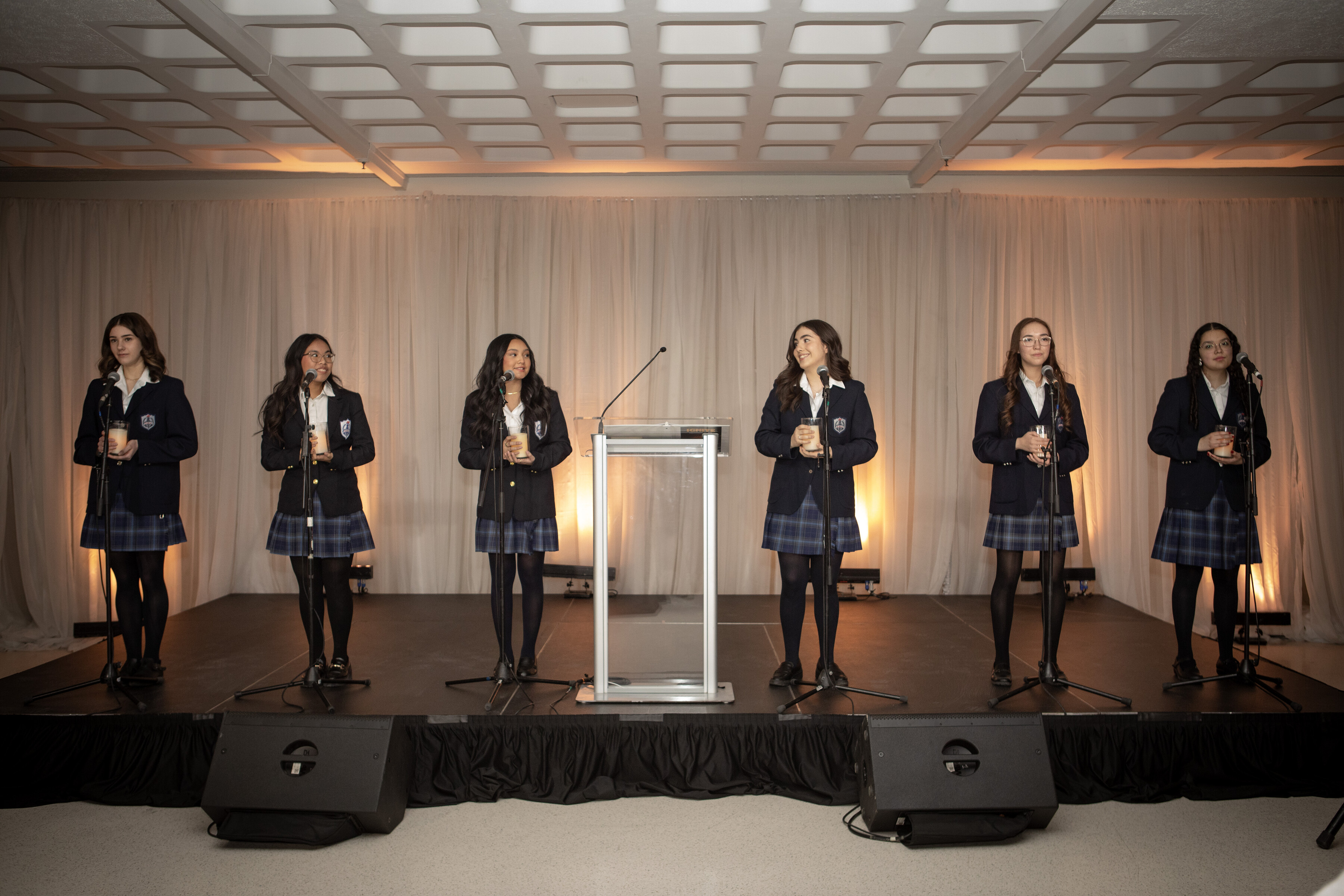 a group of SMA students holding candles and singing on a small platform