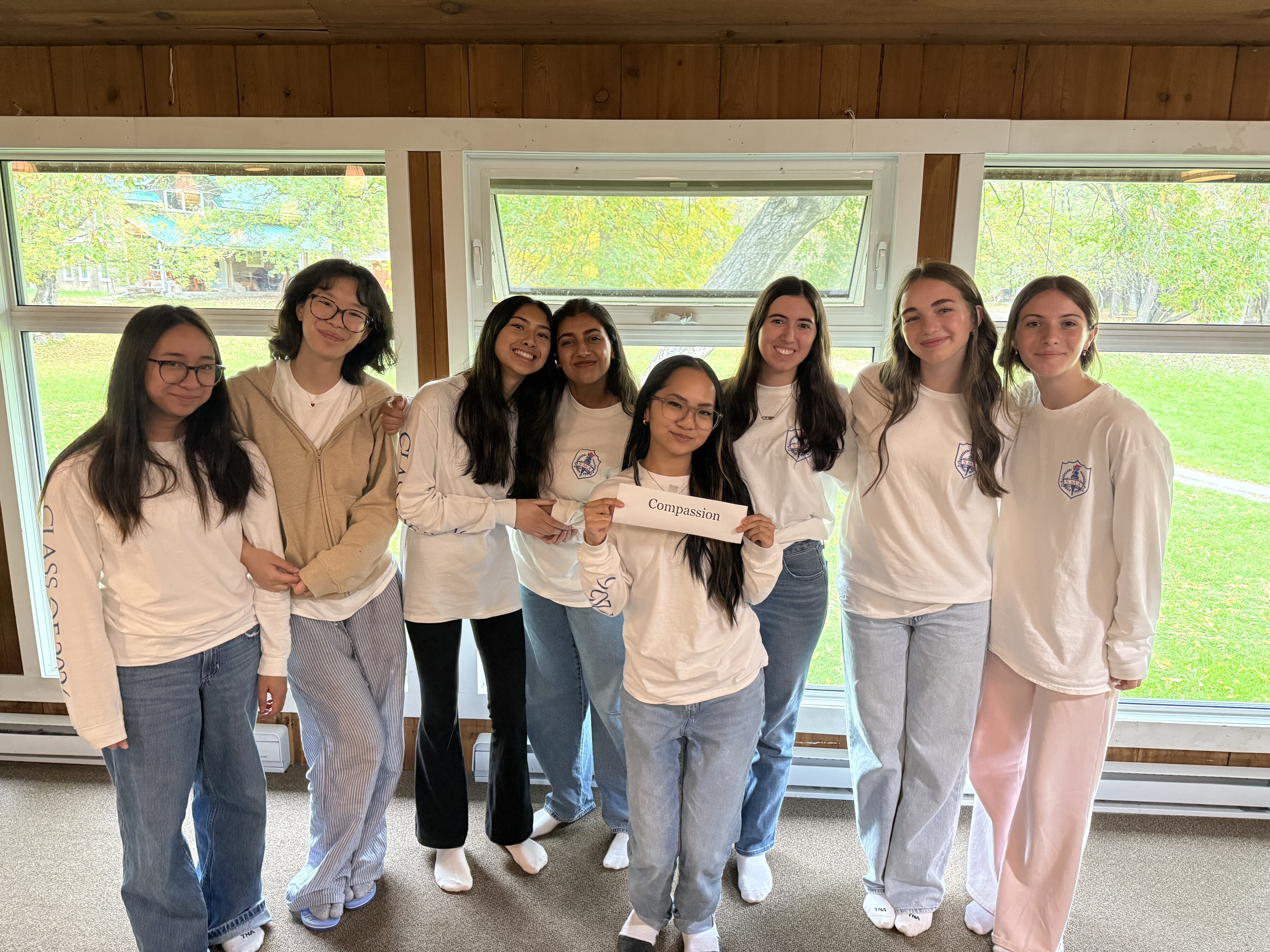 A group of St. Mary's Academy students wearing white, standing and smiling while the middle girl holds up a sign