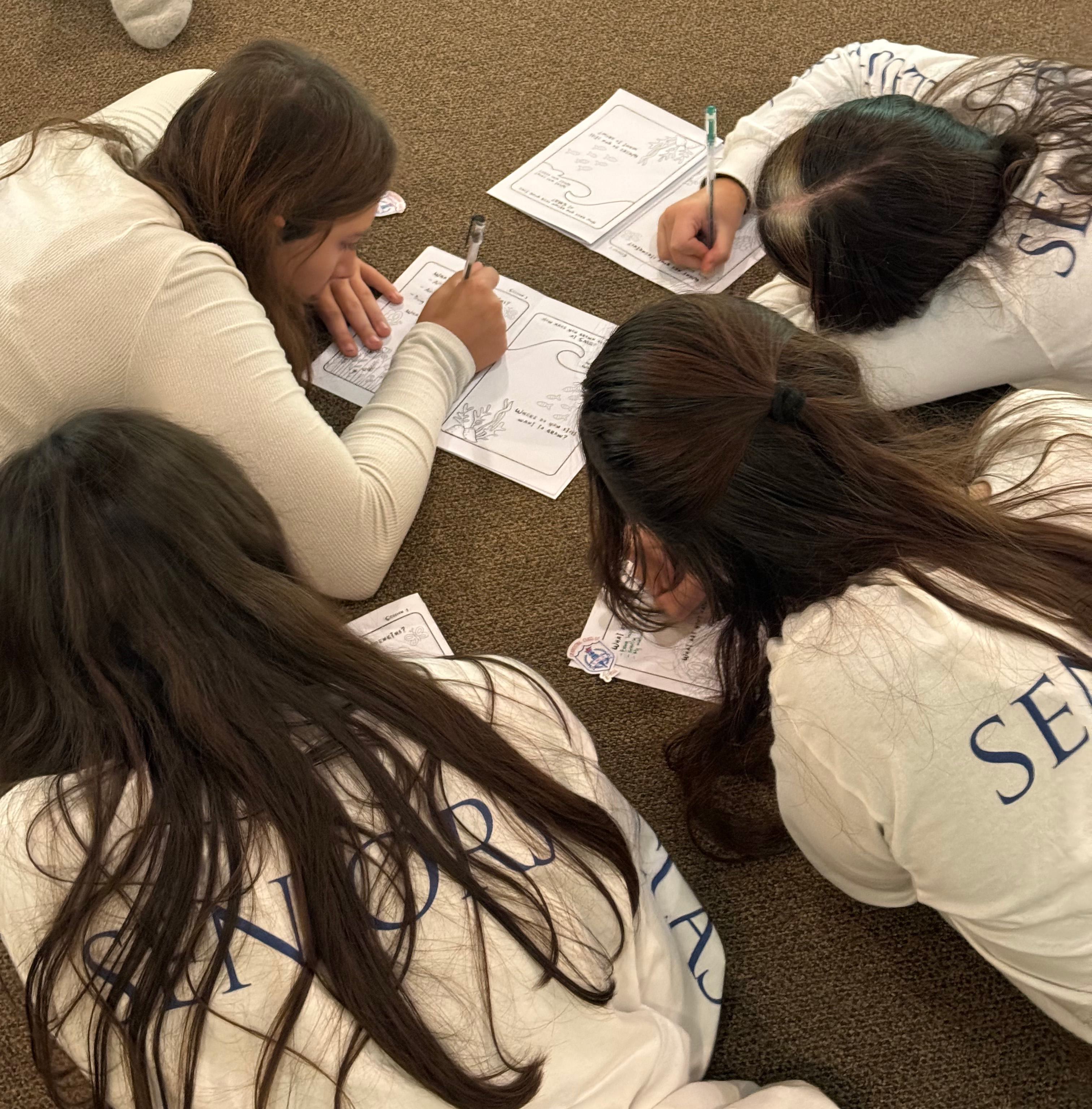 A group of St. Mary's Academy students laid down on the floor while writing on a piece of paper